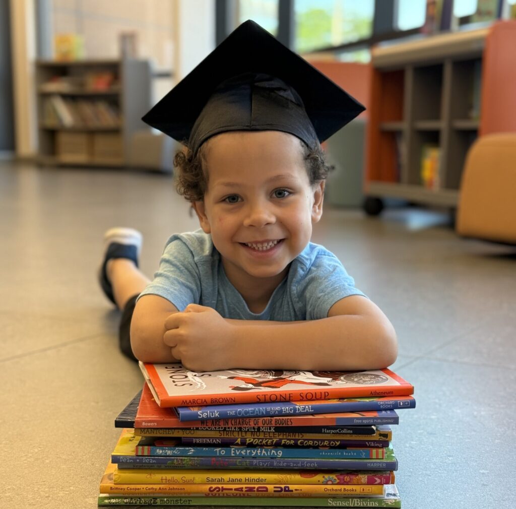 Child wearing graduation cap resting on books
